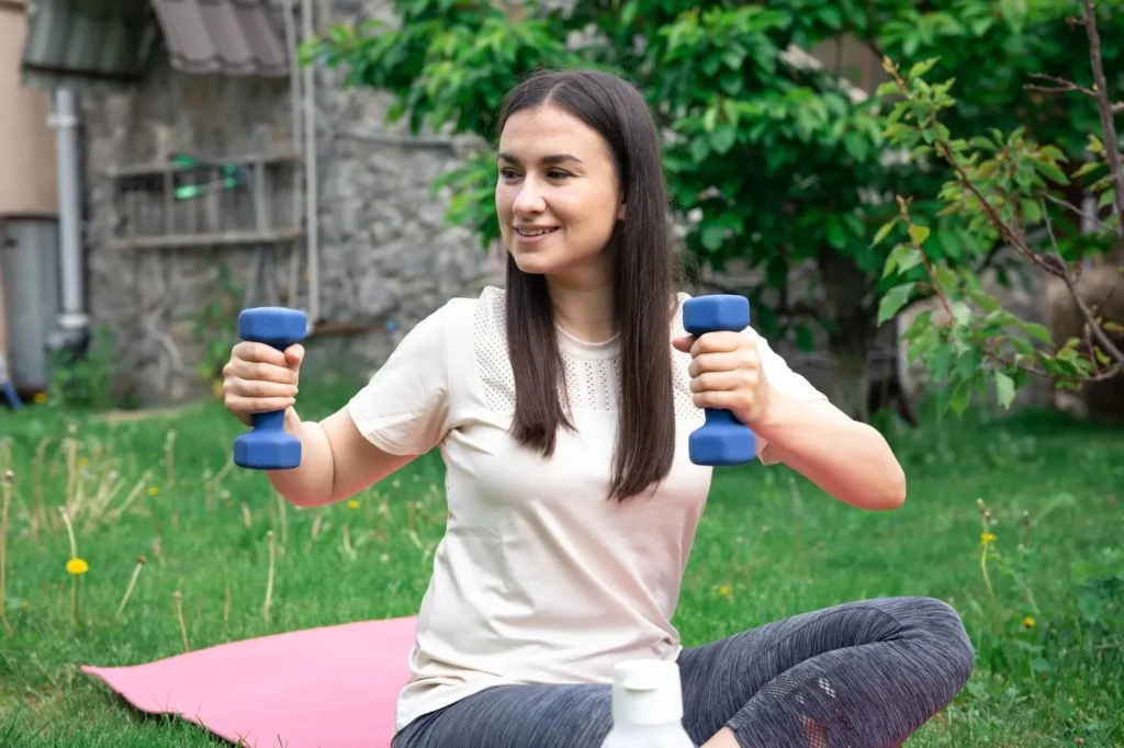 Woman stretching with dumbbells in a park, illustrating hydration and recovery after exercise