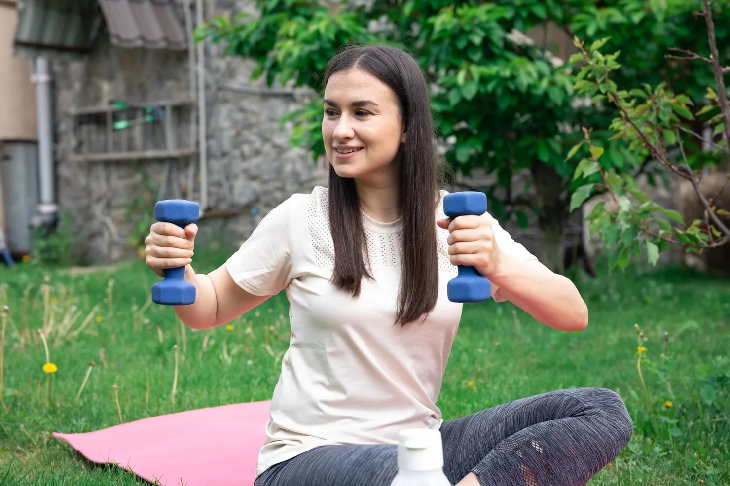 Woman stretching with dumbbells in a park, illustrating hydration and recovery after exercise